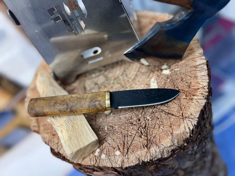 Messerfieber Nordic Grain Puukko mit Maßerpappelgriff neben einem Beil auf einem Holzblock beim Schnitzen und Holzarbeiten im Outdoor-Einsatz